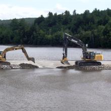 Excavators positioning rocks to create dam